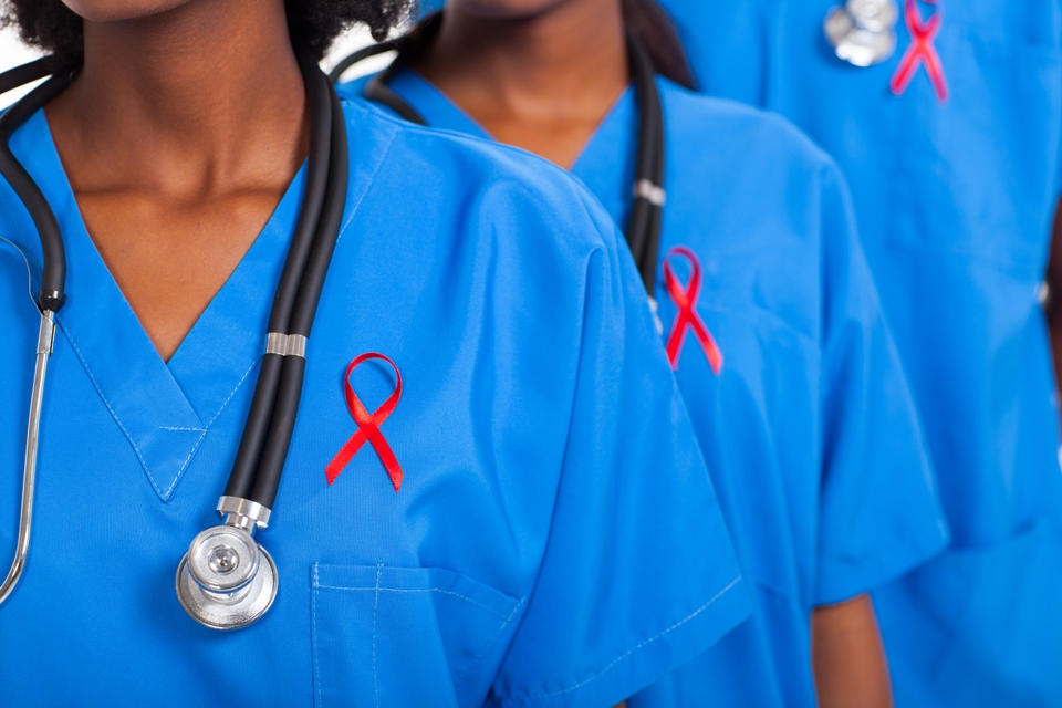 Close up of upper bodies of 3 medical professionals wearing red ribbons on their shirts.