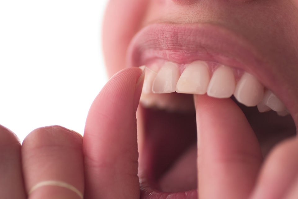 Close up of person opening their mouth and flossing their teeth.