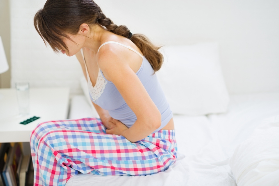 Profile of woman sitting on the side of a bed holding her stomach.