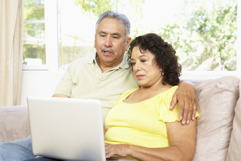 Older couple sitting together on sofa looking at a laptop together.