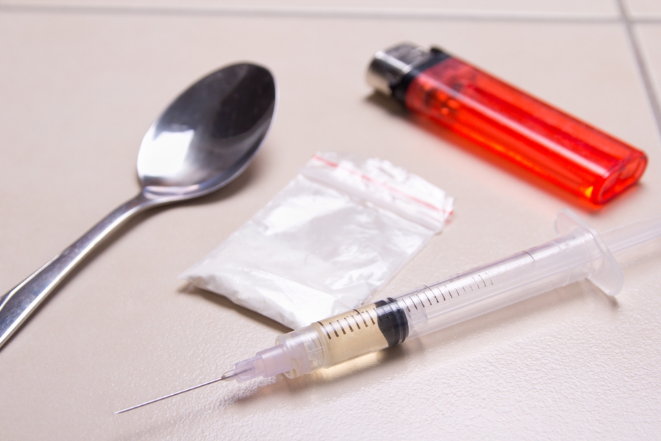 Spoon, clear bag of white powder, syringe with liquid inside it, and red lighter on a counter.
