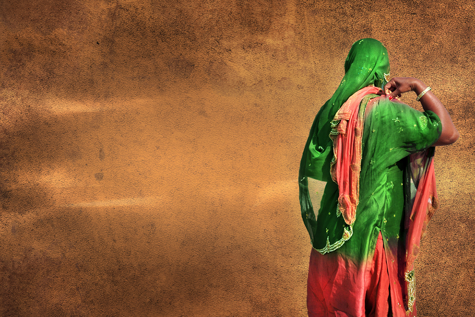 Back of woman in sari walking past a wall.