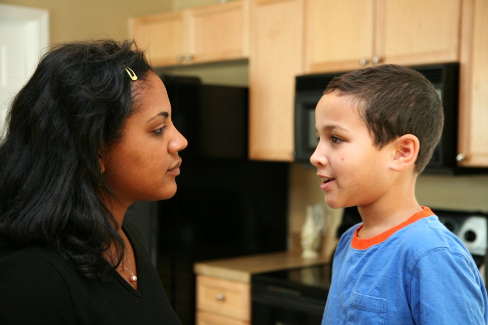Little boy and young woman talking in a kitchen.