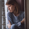 Woman sitting looking out the window crossing her arms around herself.