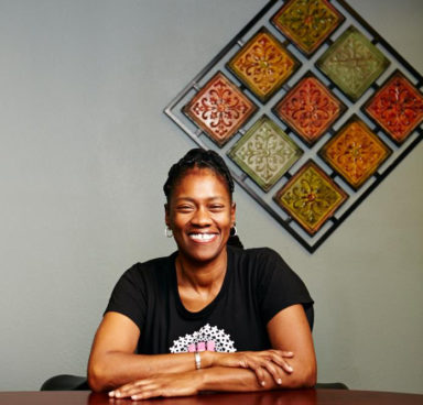 Gina Brown, RSW, smiling, sitting with arms crossed at table in front of wall art.