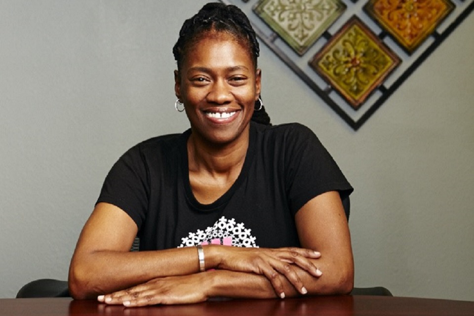 Gina Brown, RSW, smiling, sitting with arms crossed at table in front of wall art.