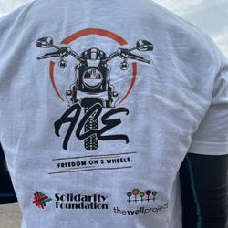 Back of t-shirt that reads "ACE, Freedom on 2 wheels" with a motorcycle and logos for The Well Project and Solidarity Foundation.