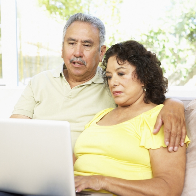 Una pareja mayor sentada en un sofá mirando una laptop juntos.