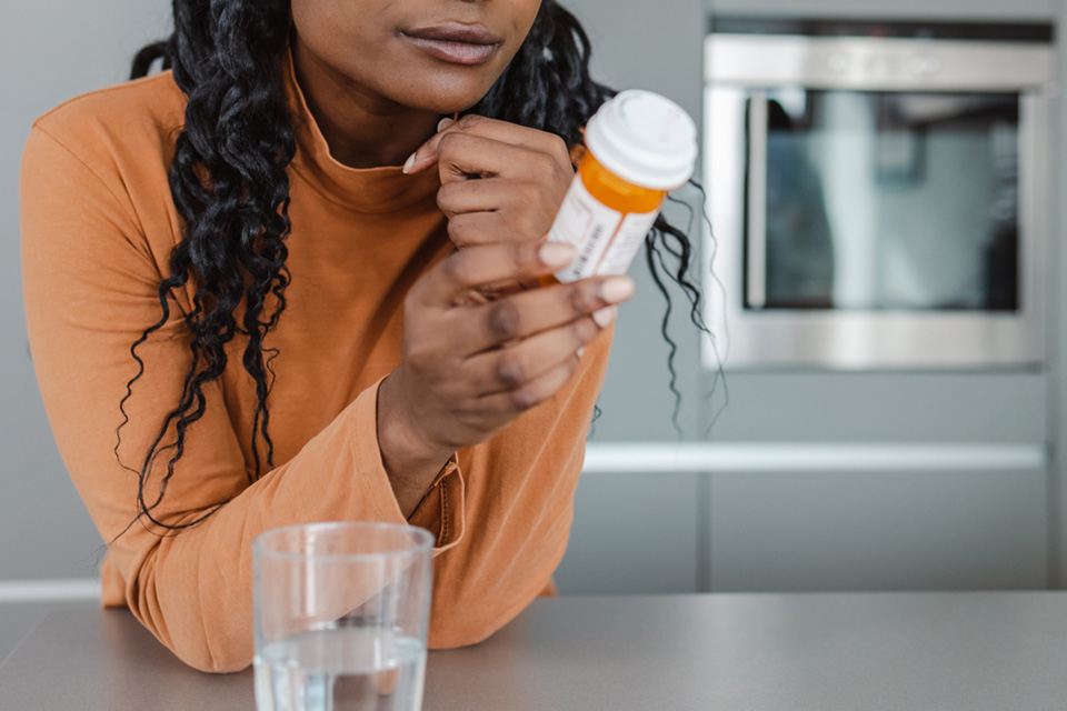 Woman reading a medicine bottle in a kitchen with a glass of water nearby.