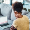 Mujer sujetándose la nuca y mirando una computadora portátil.