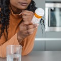 Woman reading a medicine bottle in a kitchen with a glass of water nearby.