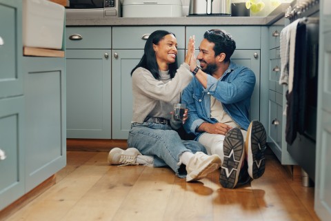 Couple sitting on kitchen floor high-fiving.